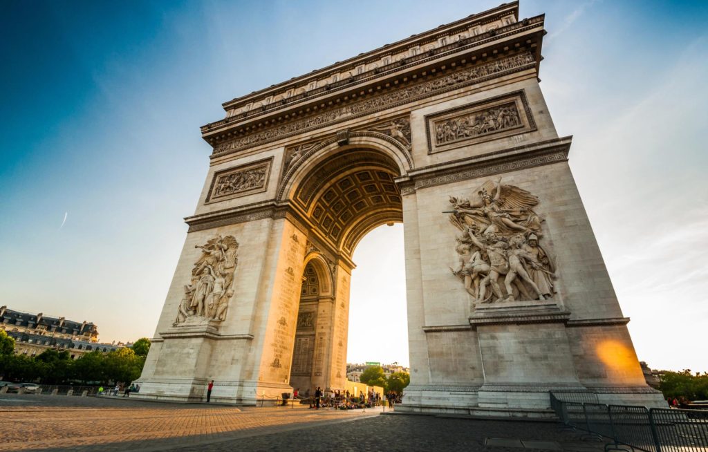The Arc de Triomphe in Paris, featuring intricate sculptures and a beautiful archway under a clear blue sky.