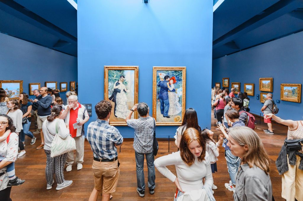 Musée d'Orsay, Paris, France. Visitors admiring artwork in an art gallery with blue walls and framed paintings.
