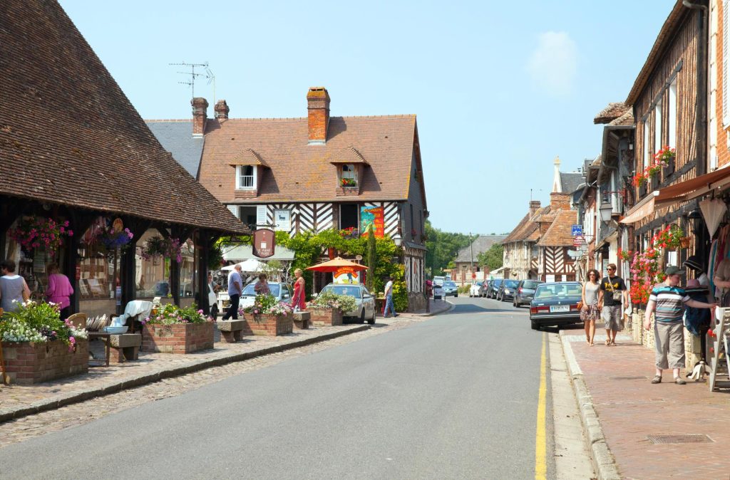 Charming street view of Beuvron-en-Auge, a picturesque village in Normandy, France, featuring half-timbered houses and vibrant flower displays.