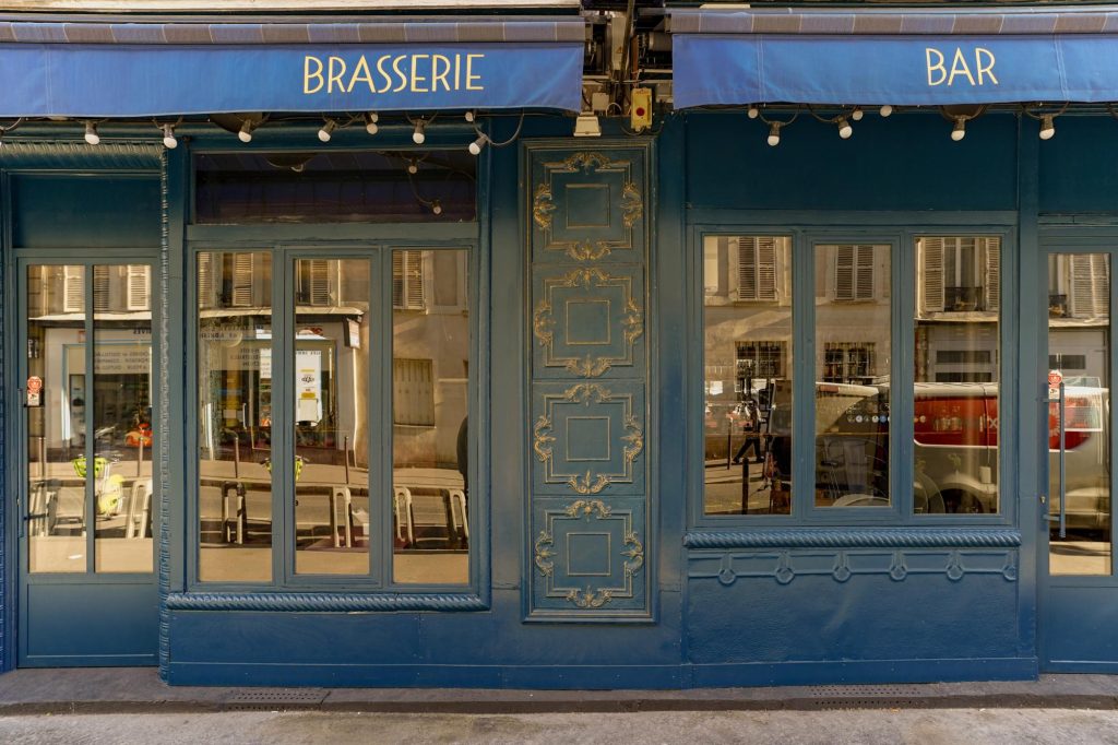Exterior view of a classic French brasserie and bar with blue paint and decorative elements.