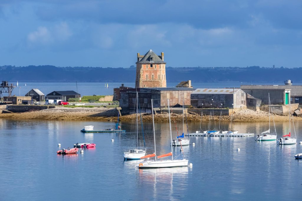 Scenic view of Camaret-sur-Mer with boats in the harbor and historic buildings in the background under a clear blue sky.