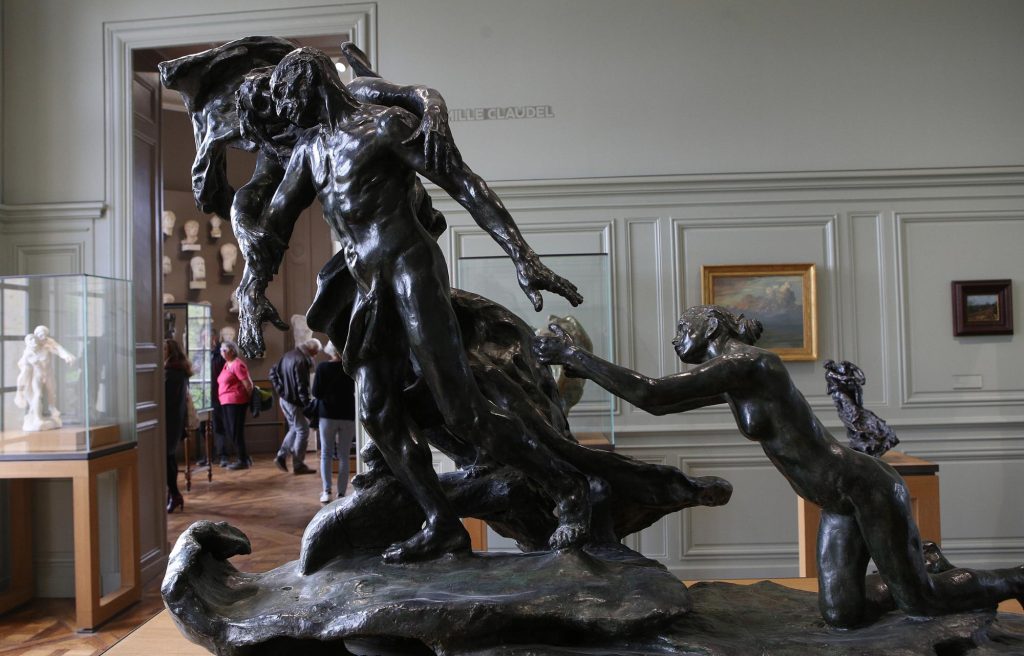A bronze sculpture by Camille Claudel depicting a dynamic scene with a male and female figure, surrounded by museum visitors and artworks.