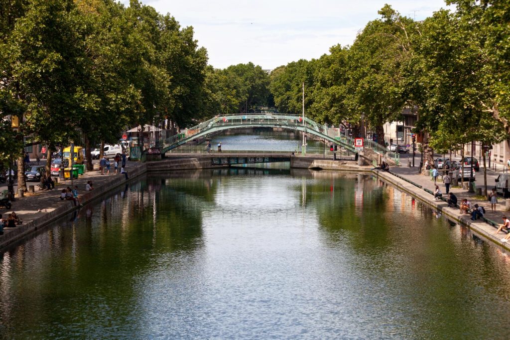 A scenic view of Canal Saint-Martin in Paris, featuring a green bridge and people relaxing by the water.