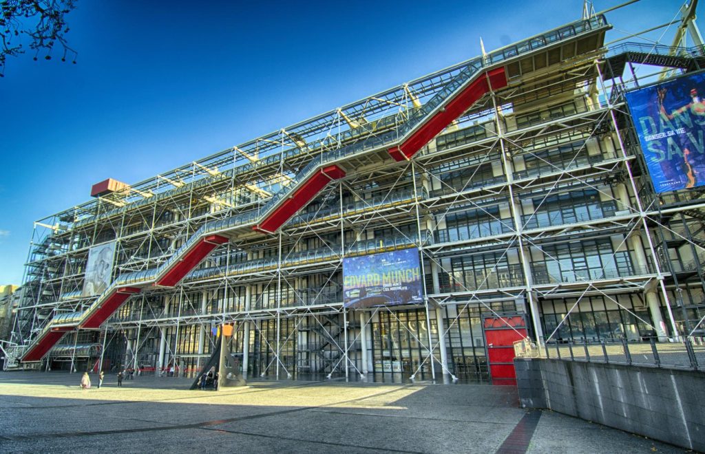 Exterior view of the Centre Pompidou in Paris, showcasing its modern architecture with red stairs and scaffolding.