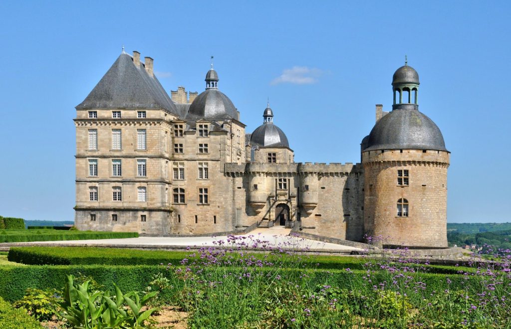 A beautiful view of the Château de Hautefort, showcasing its grand architecture and landscaped gardens under a clear blue sky.