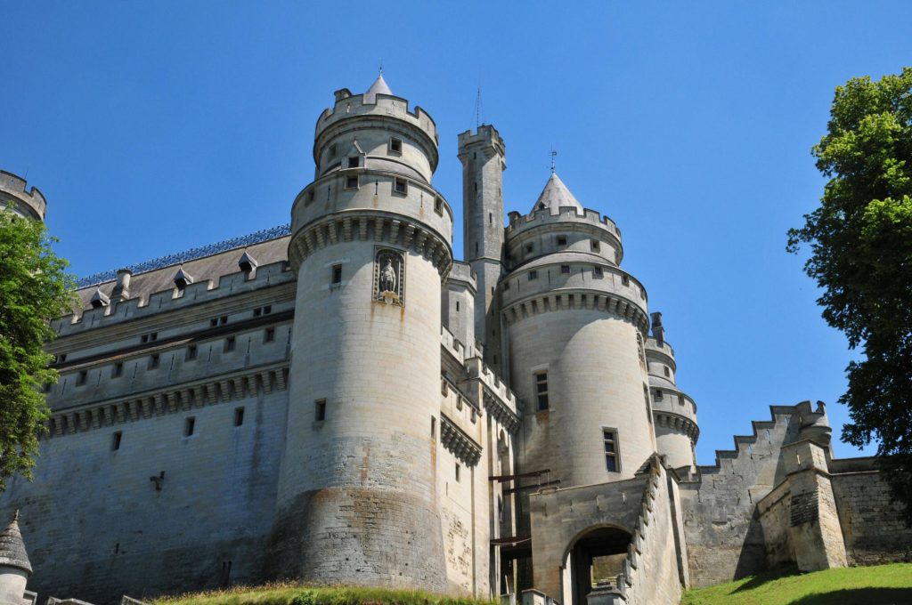 A view of the Château de Pierrefonds featuring its large stone towers and battlements against a clear blue sky.