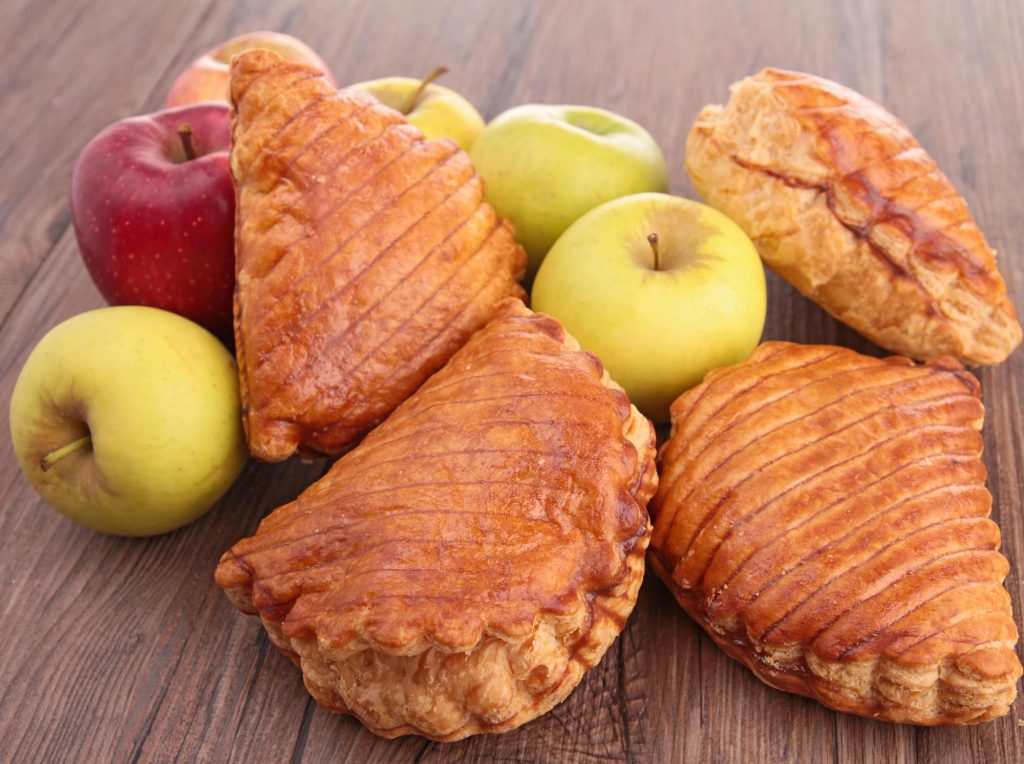 A delicious apple turnover pastry surrounded by fresh apples, showcasing a golden-brown flaky crust.