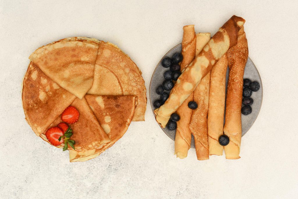 A plate of crêpes topped with fresh strawberries and blueberries, showcasing a delightful breakfast dish.