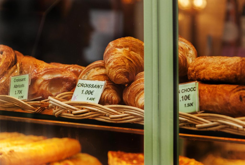 A variety of fresh croissants displayed in a bakery window, including plain and fruit-filled options, with price tags visible.