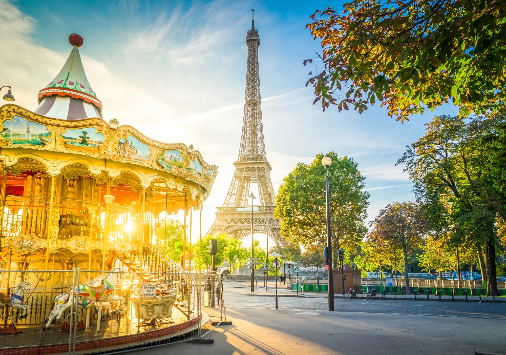 A scenic view of the Eiffel Tower in Paris during sunset, with a traditional carousel featuring painted horses in the foreground.