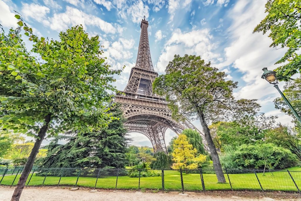 A view of the Eiffel Tower surrounded by lush greenery and trees under a cloudy sky in Paris.