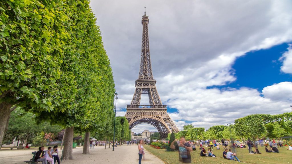 The Eiffel Tower surrounded by lush greenery with visitors enjoying the park on a cloudy day.