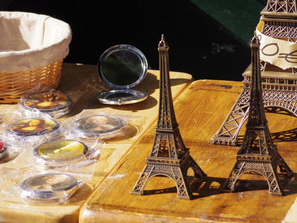 A display of Eiffel Tower souvenirs and compact mirrors featuring famous artworks on a wooden table.