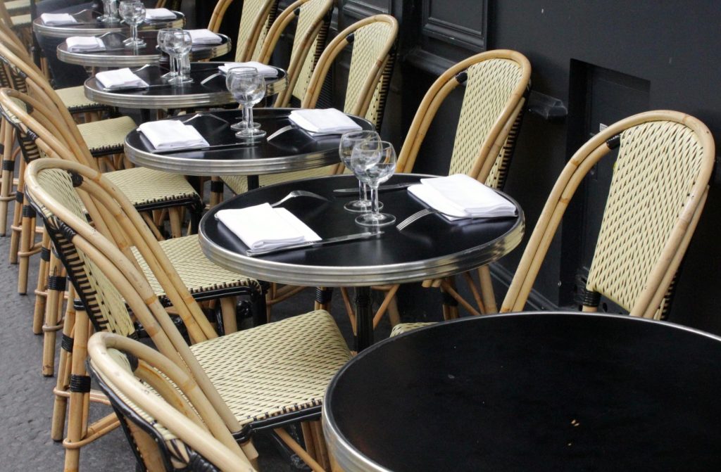 Empty round tables and chairs at a Parisian cafe, set with cutlery and glassware, ready for diners.