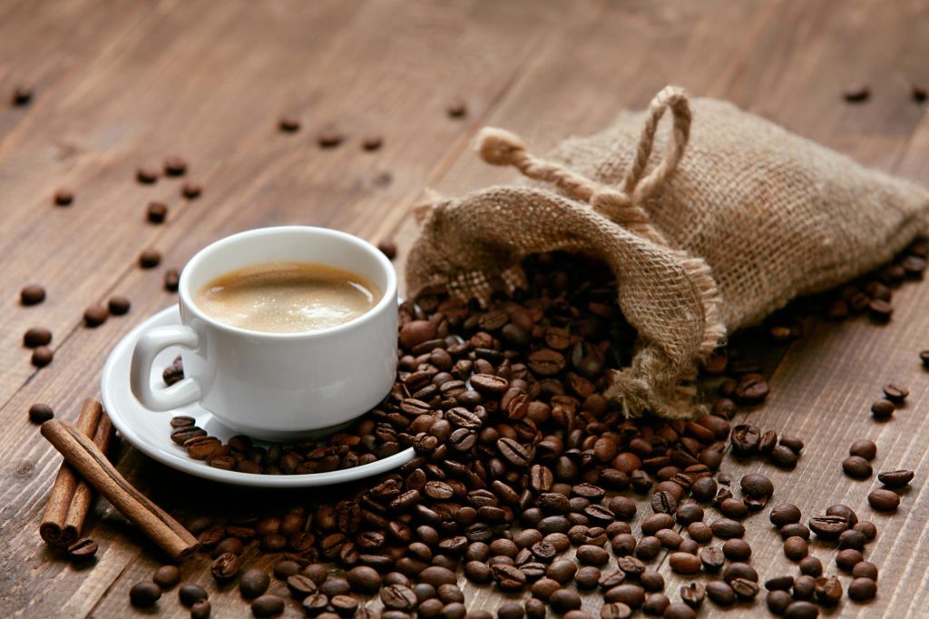 A cup of espresso surrounded by coffee beans and a burlap sack on a wooden surface.