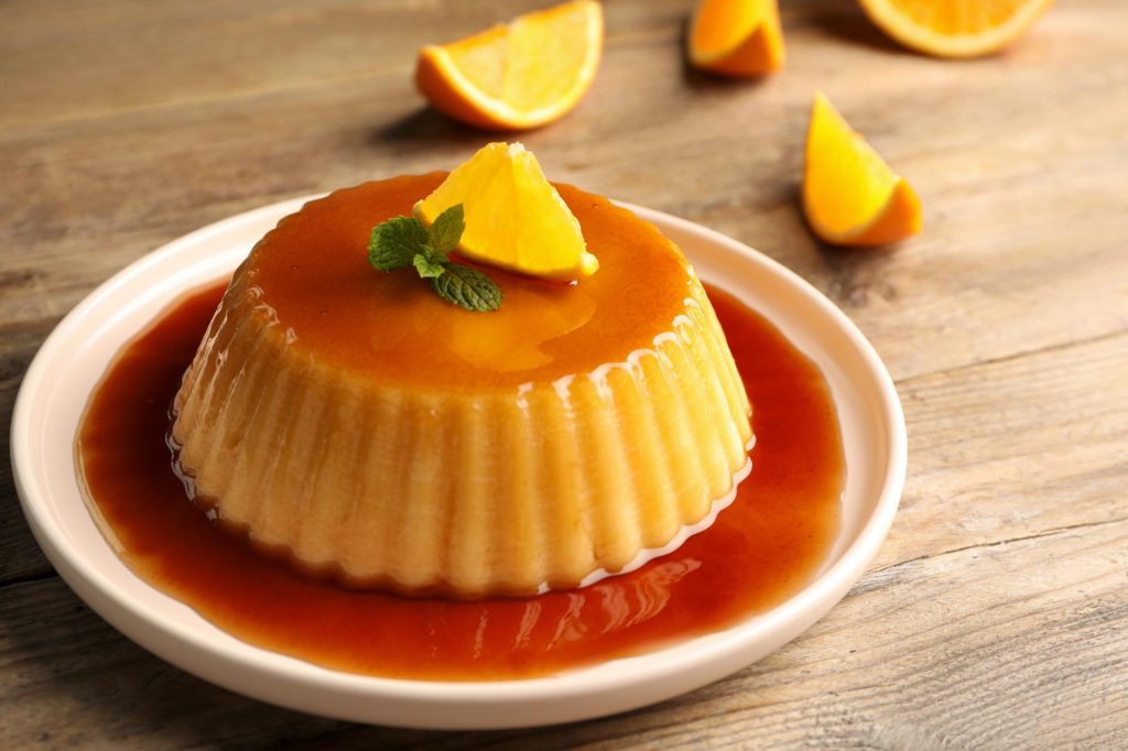 A delicious Parisian flan topped with a slice of orange and mint leaves, served on a wooden table.
