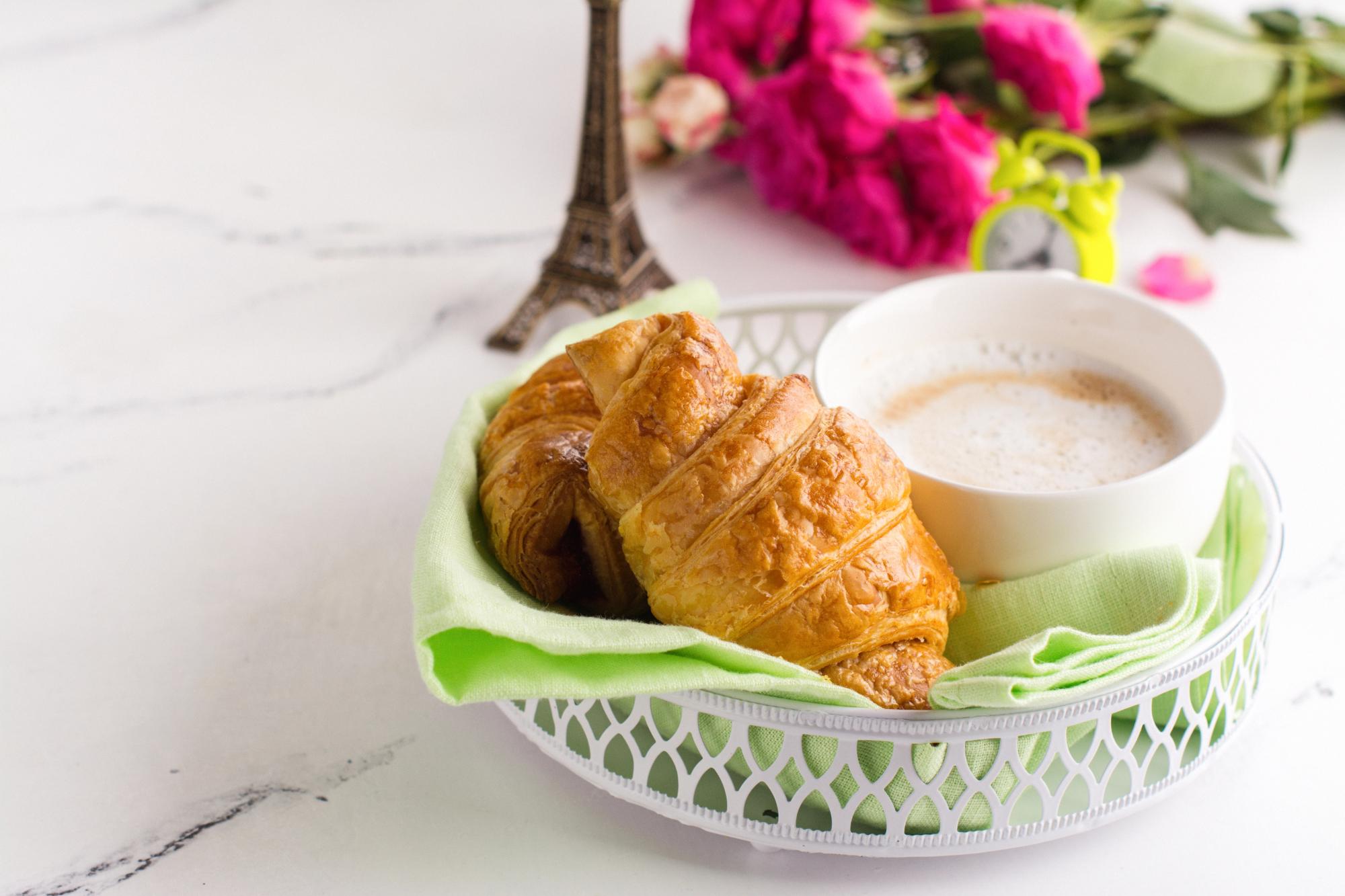 a plate with a croissant and a cup of coffee, surrounded by flowers