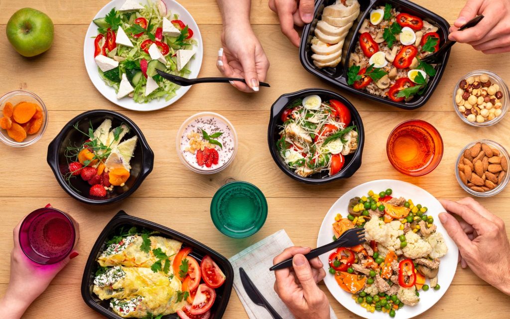 A top view of a healthy lunch spread including various salads, fruits, and drinks, featuring colorful vegetables and fresh ingredients.