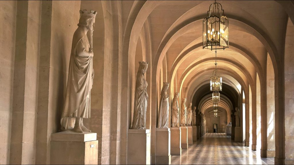 A beautiful corridor featuring arched architecture with statues of royal figures, illuminated by hanging lanterns.