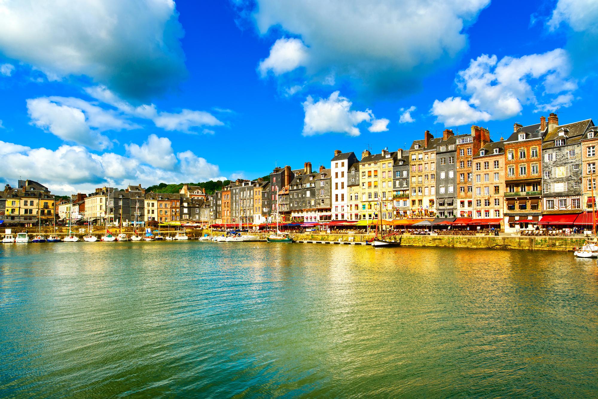 Scenic view of Honfleur harbor with colorful buildings and boats under a blue sky with clouds.