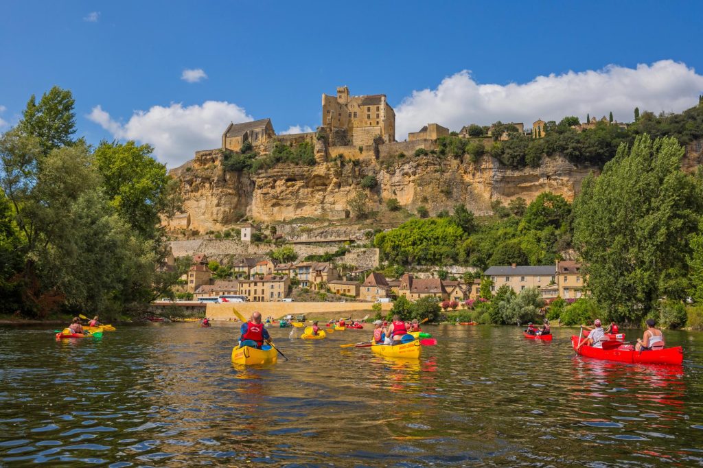 Colorful kayaks on the Dordogne River with a scenic backdrop of cliffs and historic buildings.
