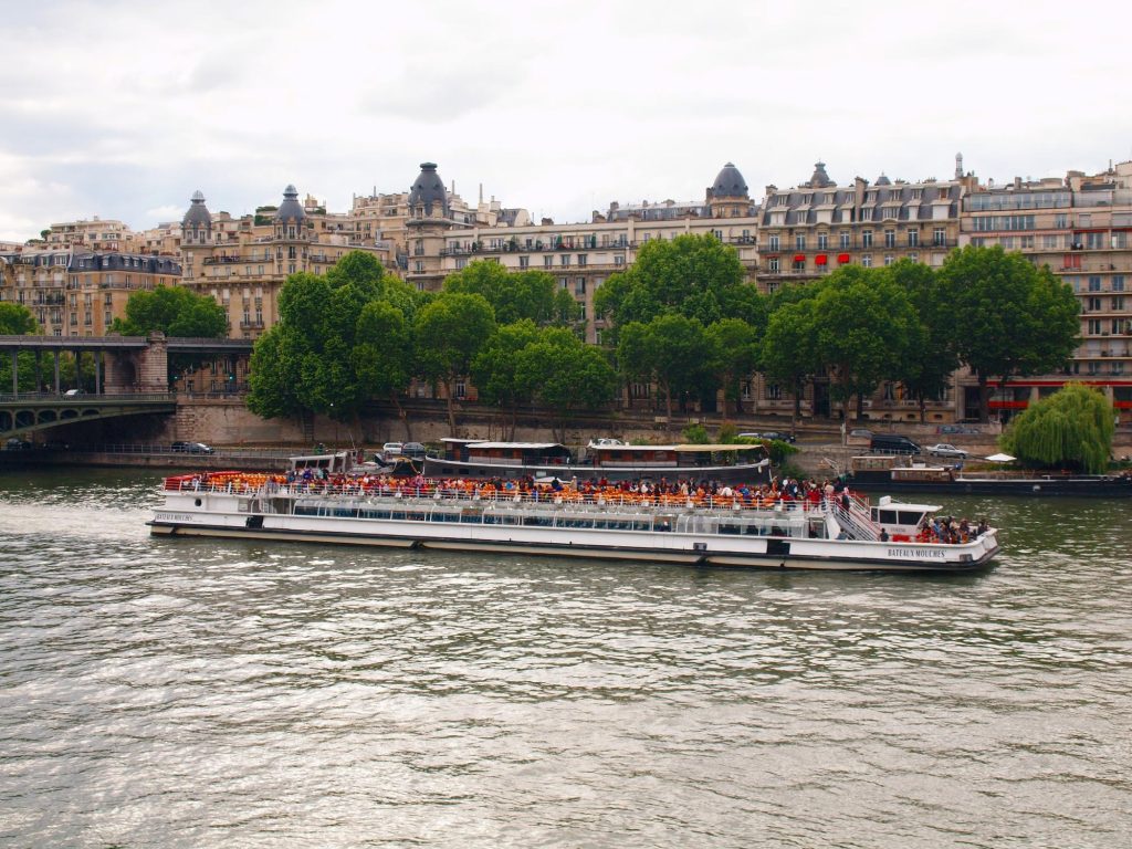 A scenic view of boats on the Seine River in Paris, with beautiful architecture and trees lining the riverbank.