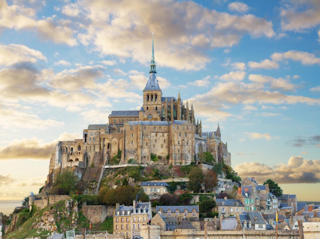 A picturesque view of Mount Saint-Michel castle with its historic architecture, surrounded by clouds and a tranquil sky.