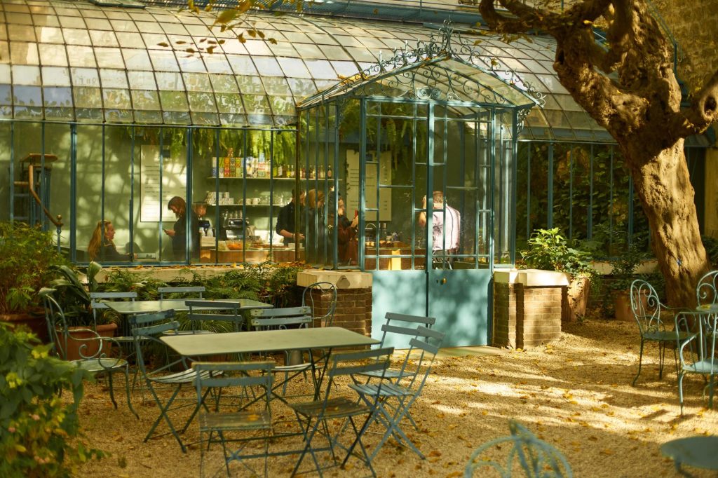 A cozy café inside the Museum of Romantic Life with green plants, blue metal chairs, and people interacting.