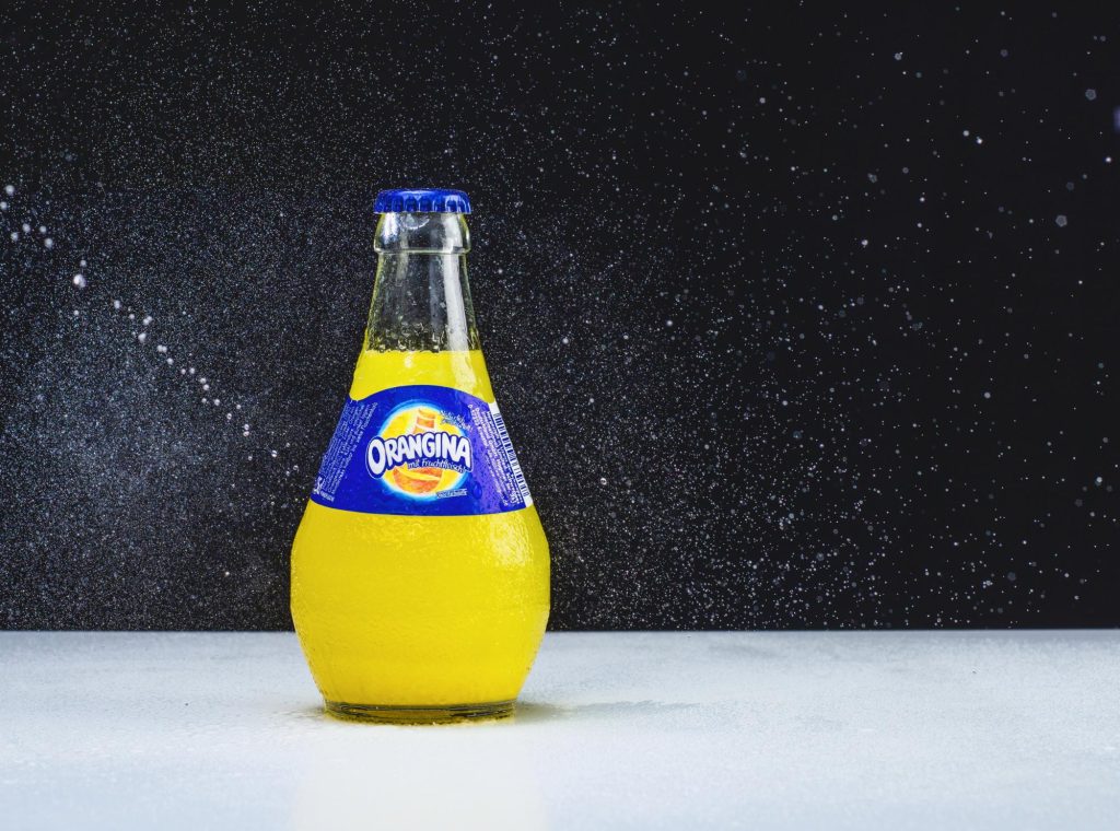 A chilled bottle of Orangina with condensation on the glass, set against a dark background with droplets of water.
