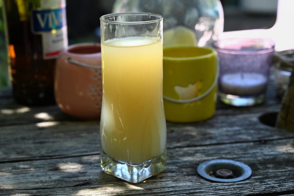 A glass of pastis, a traditional French anise-flavored spirit, served on a wooden table with colorful background items.