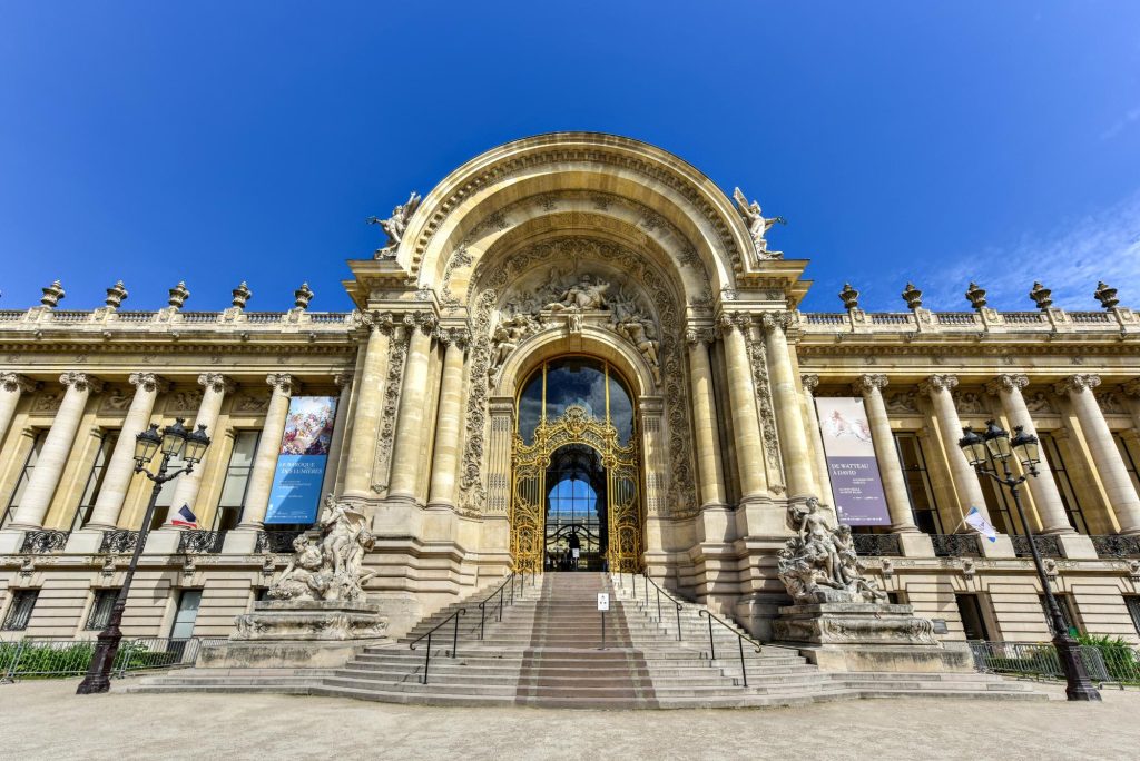 The ornate entrance of the Petit Palais museum in Paris, showcasing intricate sculptures and golden details against a clear blue sky.