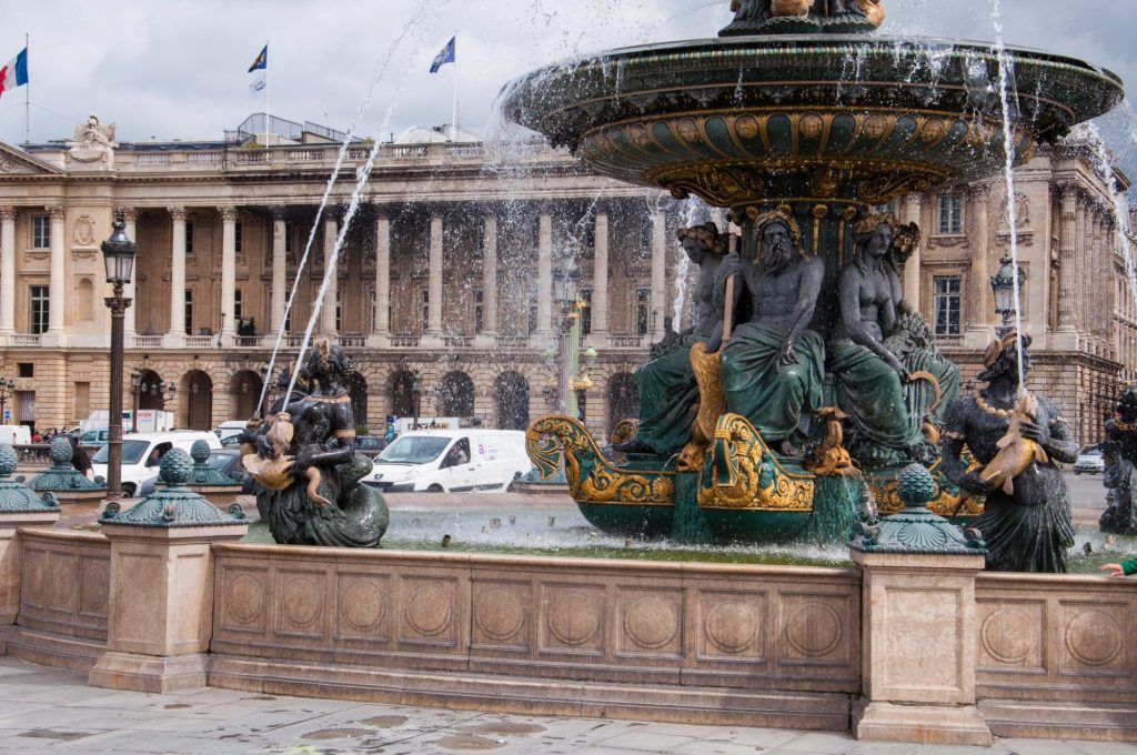 A detailed view of the fountain at Place de la Concorde in Paris, showcasing intricate sculptures and flowing water with historical architecture in the background.