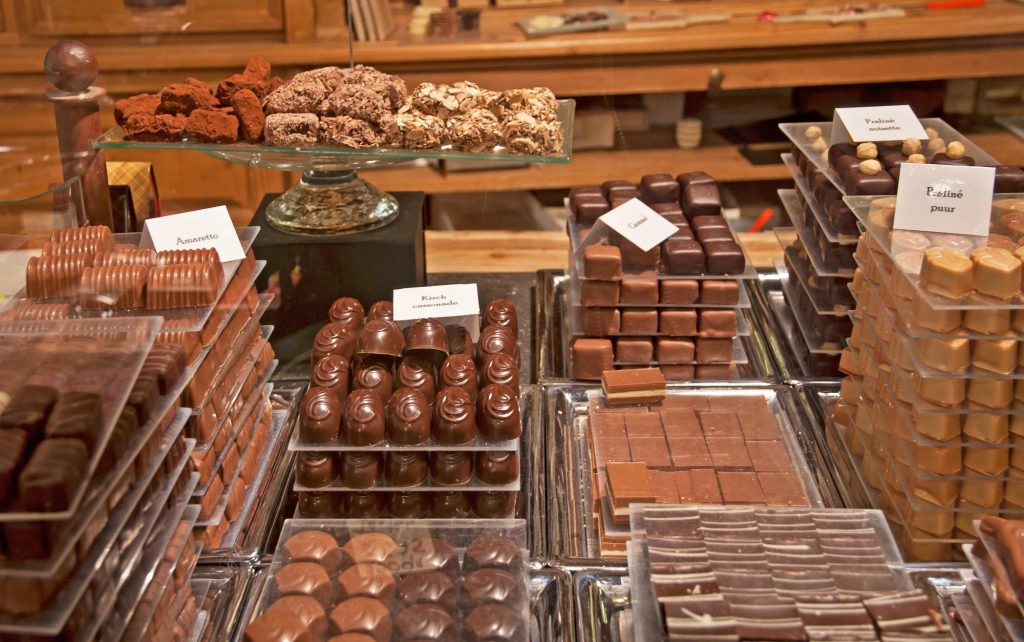 A display of assorted chocolates including raspberry and basil ganache, with various shapes and flavors showcased in elegant packaging.