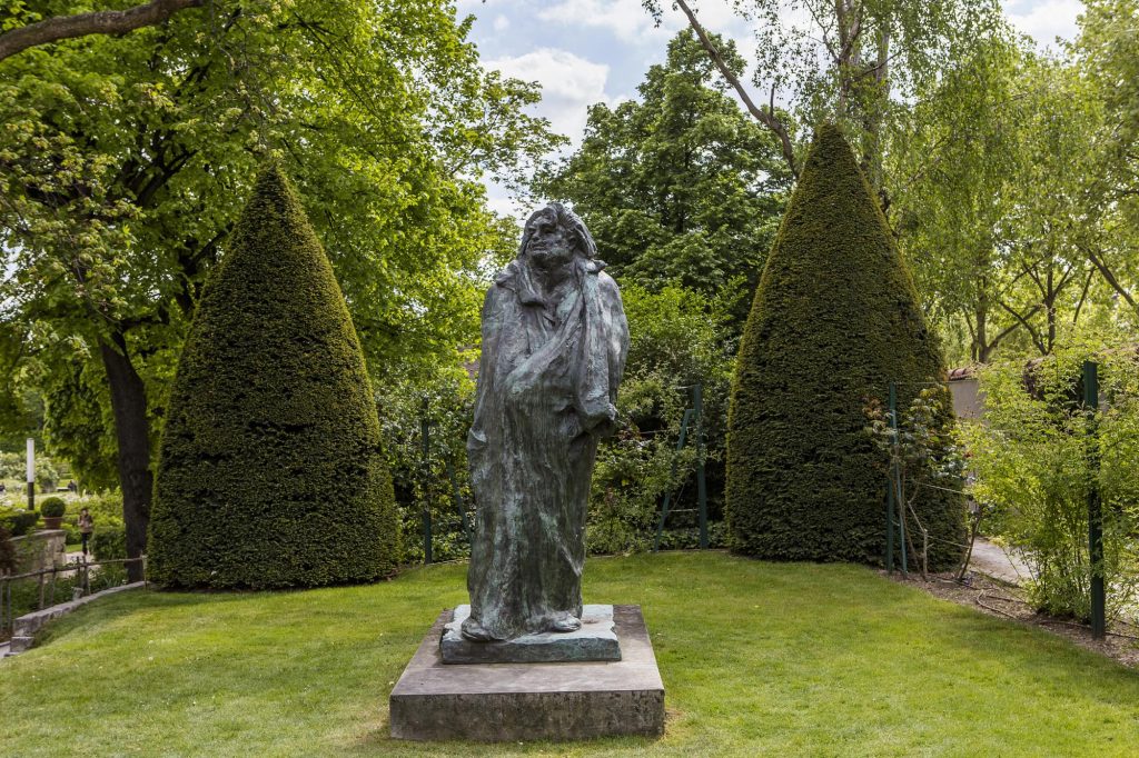 A bronze statue in the gardens of the Rodin Museum surrounded by lush greenery and trimmed hedges.