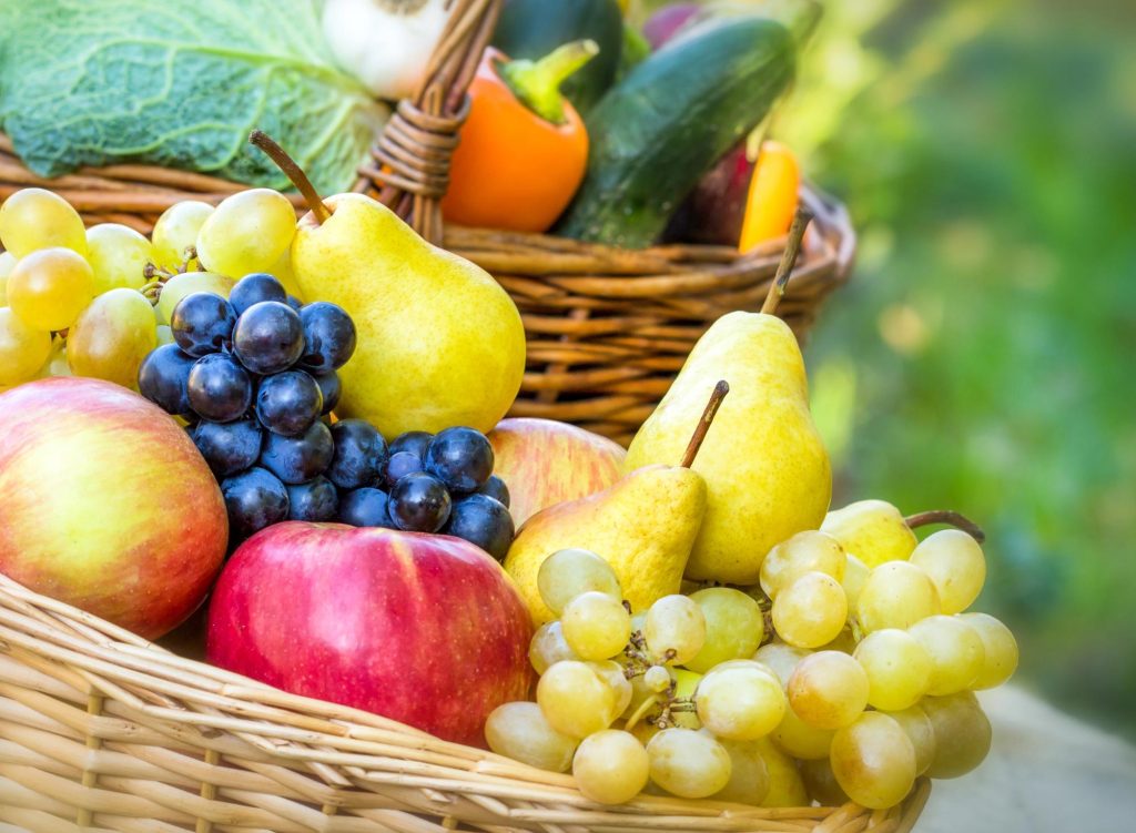A vibrant assortment of seasonal fruits including apples, pears, grapes, and yellow grapes arranged in a woven basket.