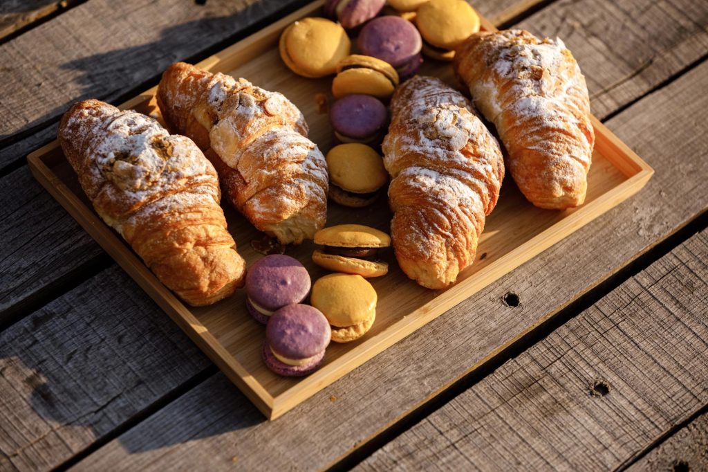 A wooden tray filled with croissants and colorful macarons, showcasing a delightful assortment of pastries.