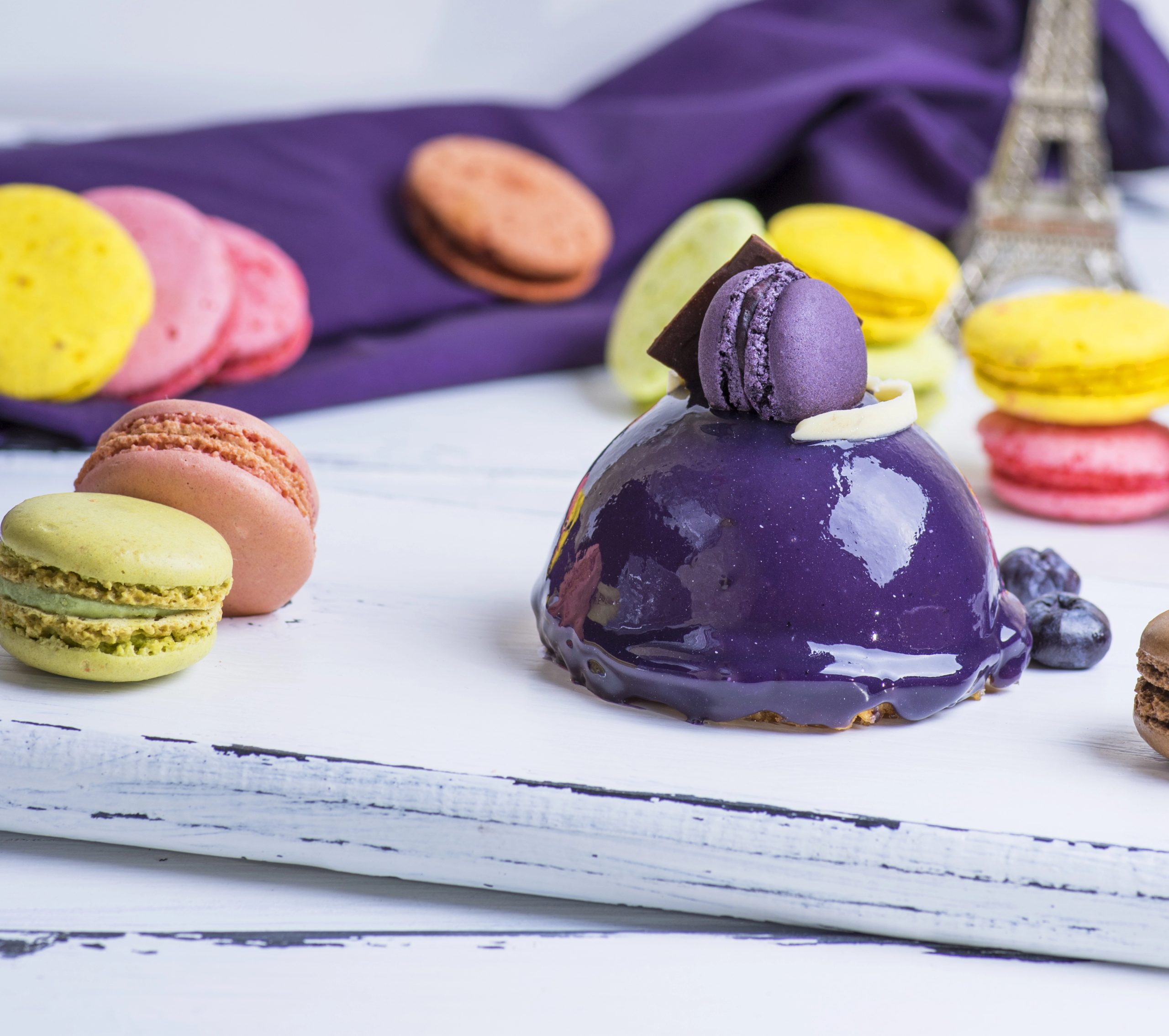 Gâteau rond lilas avec macarons sur une planche en bois blanc, gros plan