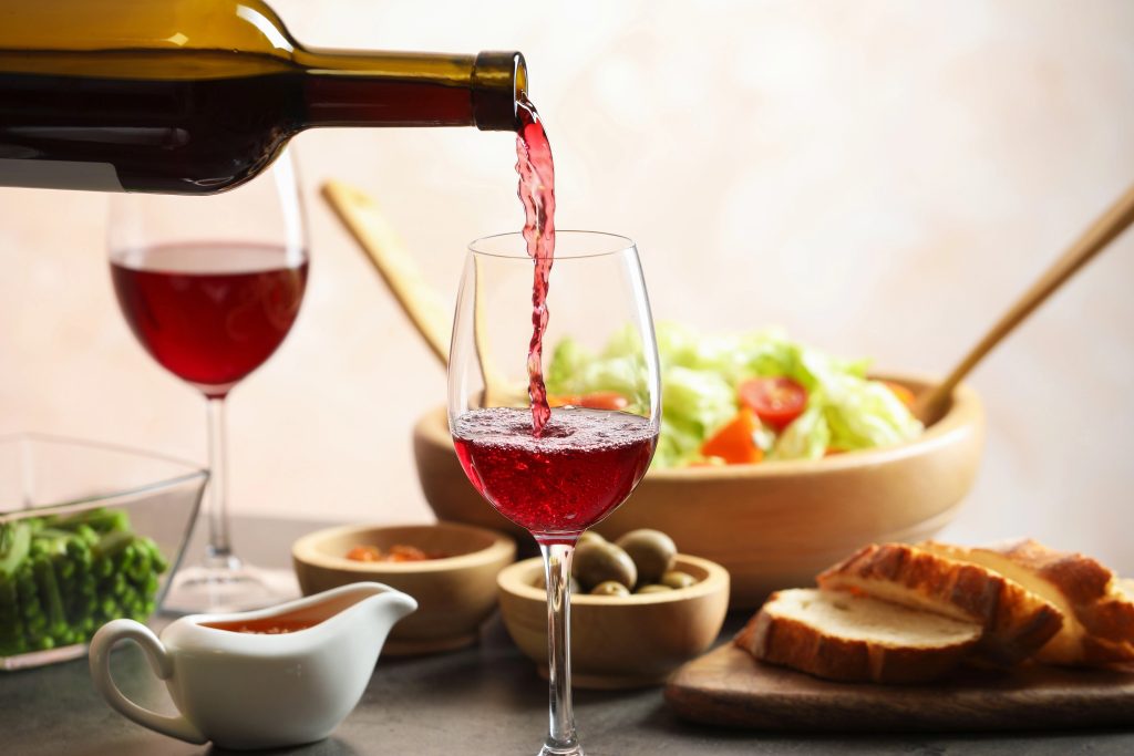 Pouring red wine into glass at grey table with tasty food
