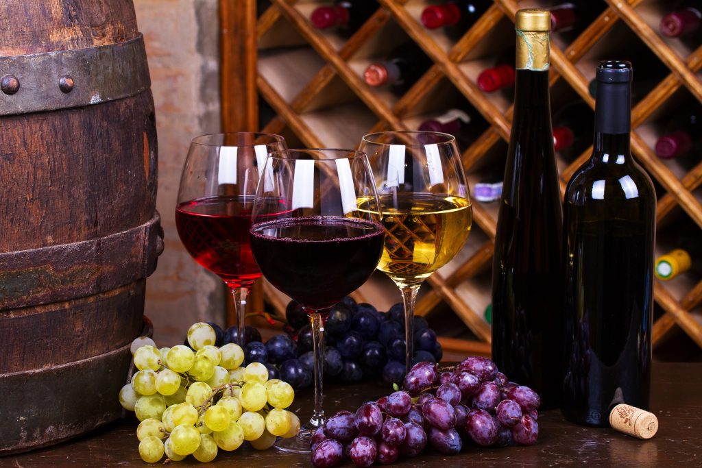 Red, rose and white glasses and bottles of wine with grapes in wine cellar