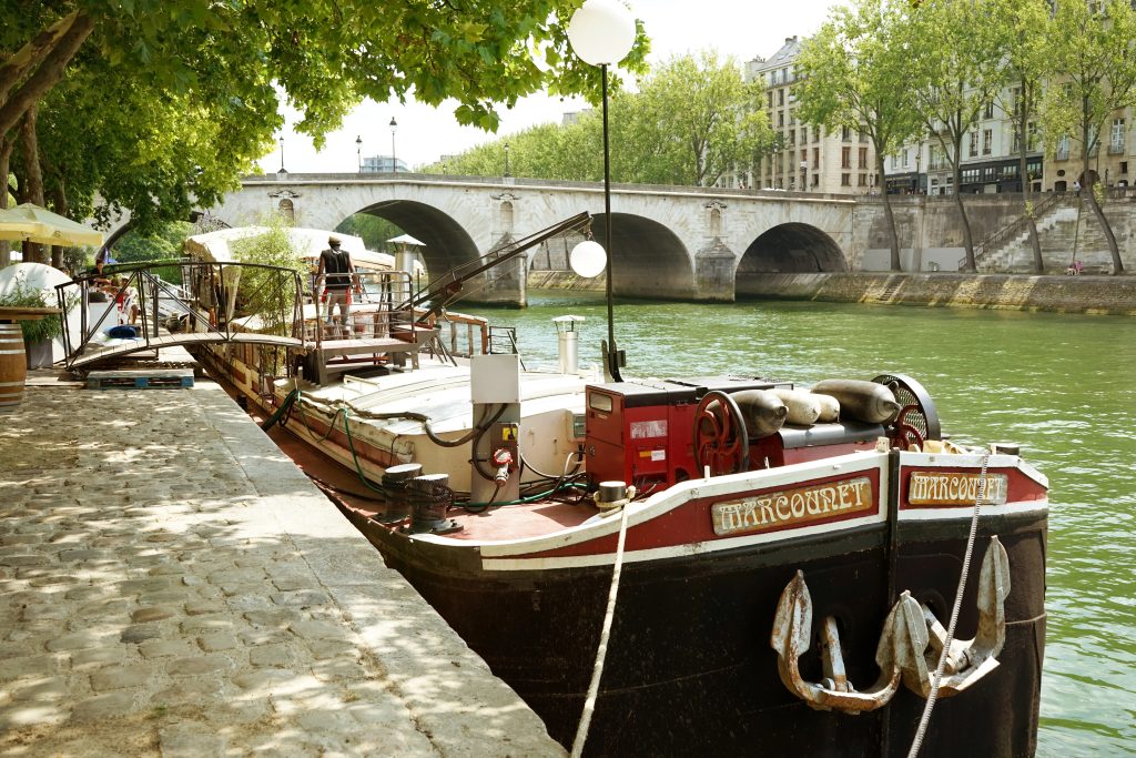 Seine riverbank near the pont Marie bridge and the Ile Saint-Louis on the right. A barge transformed into a restaurant. Summer in Paris, France. 