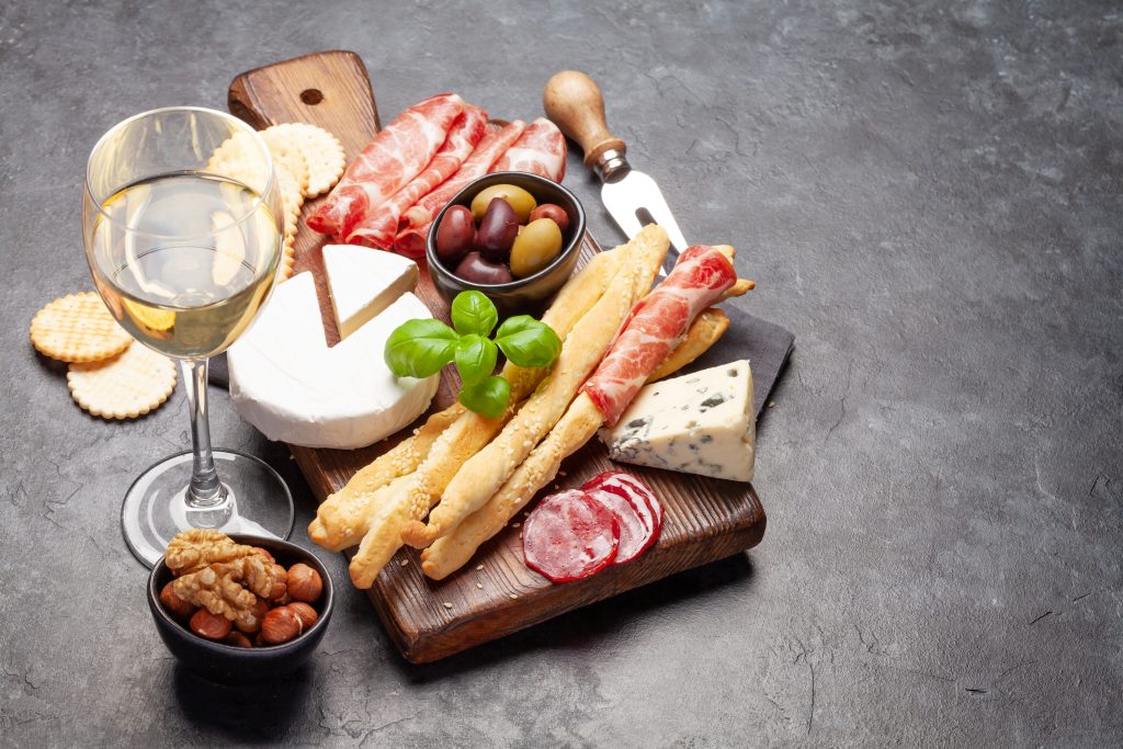 Cheese, meat, grapes and nuts antipasto. Appetizer selection on plate and glass with white wine. With copy space