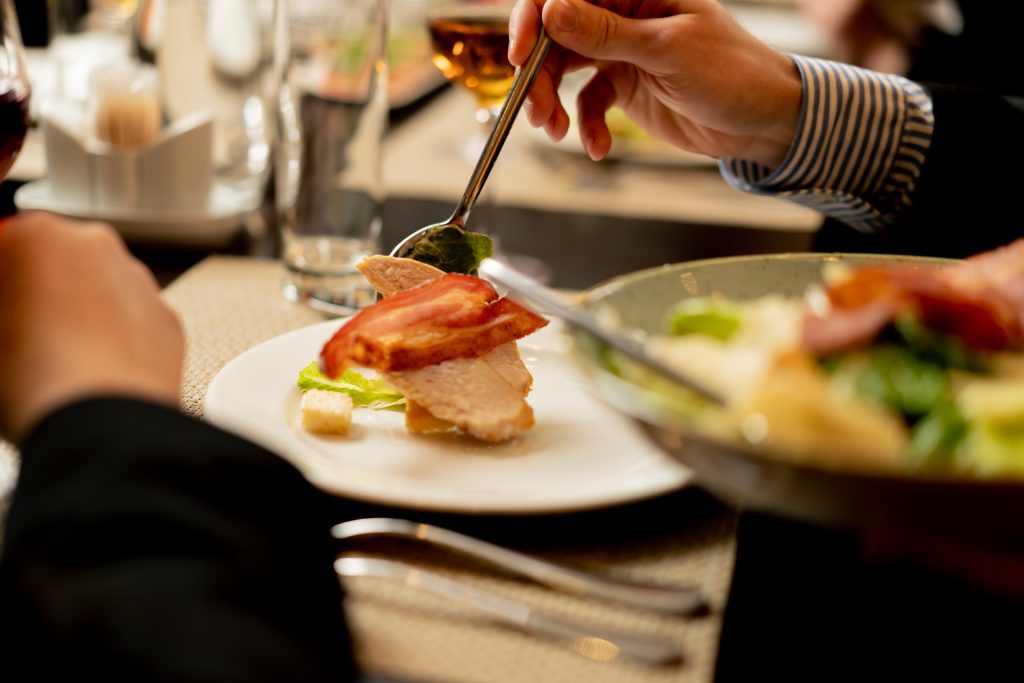 close-up of a person in a restaurant putting a salad on a plate on servery table
