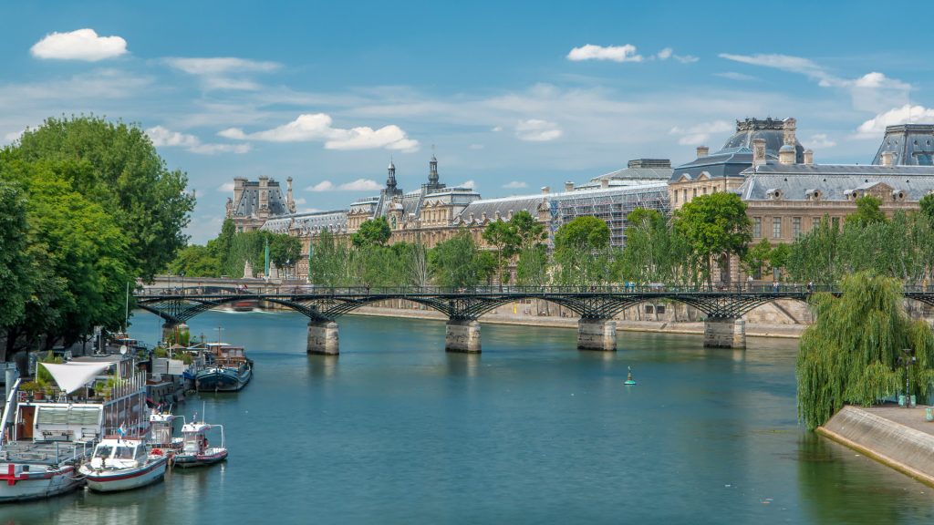Touristic boat passes below Pont des Arts, on boat station on Seine river timelapse in Paris. Louvre museum on background. Paris is the top touristic destination in Europe.