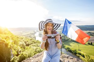 Young happy woman tourist with photo camera and french flag traveling near the Domme village in France