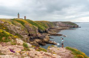 A young tourist on the coast next to the Phare Du Cap Frehel, is a maritime lighthouse in Cotes de Armor (France). At the tip of Cap Frehel