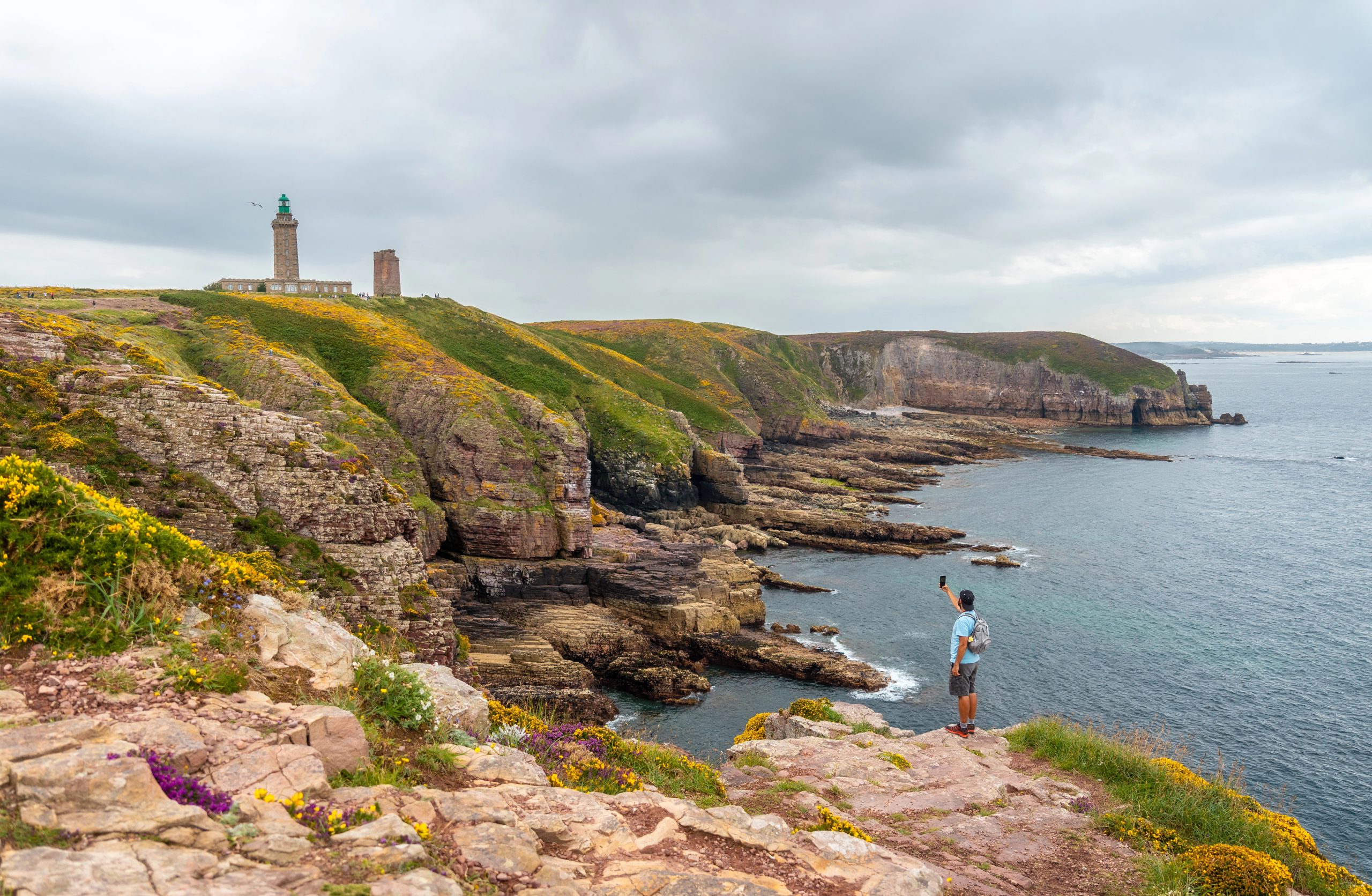 A young tourist on the coast next to the Phare Du Cap Frehel, is a maritime lighthouse in Cotes de Armor (France). At the tip of Cap Frehel
