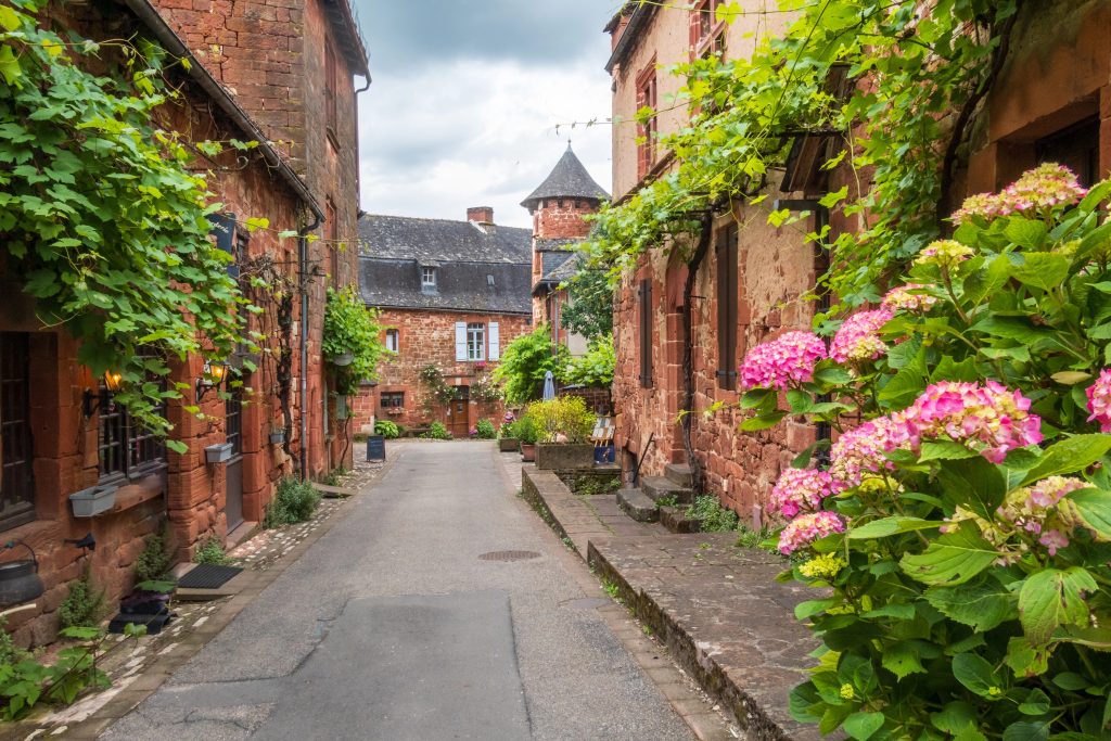 Facades of red stone houses and green plants seen from the street in Collonges-la-Rouge, Correze, France.