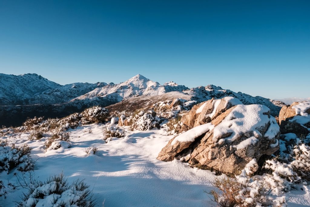 A rocky outcrop covered in snow in front of the snow covered peak of Monte San Parteo lit up by the early orning sun in the Balagne region of Corsica